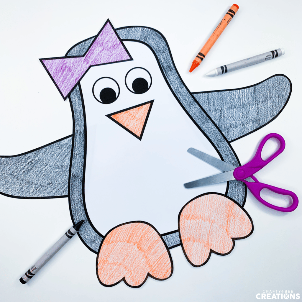 This female penguin craft has been colored black, white and orange by a student. There are purple scissors and crayons lying nearby.