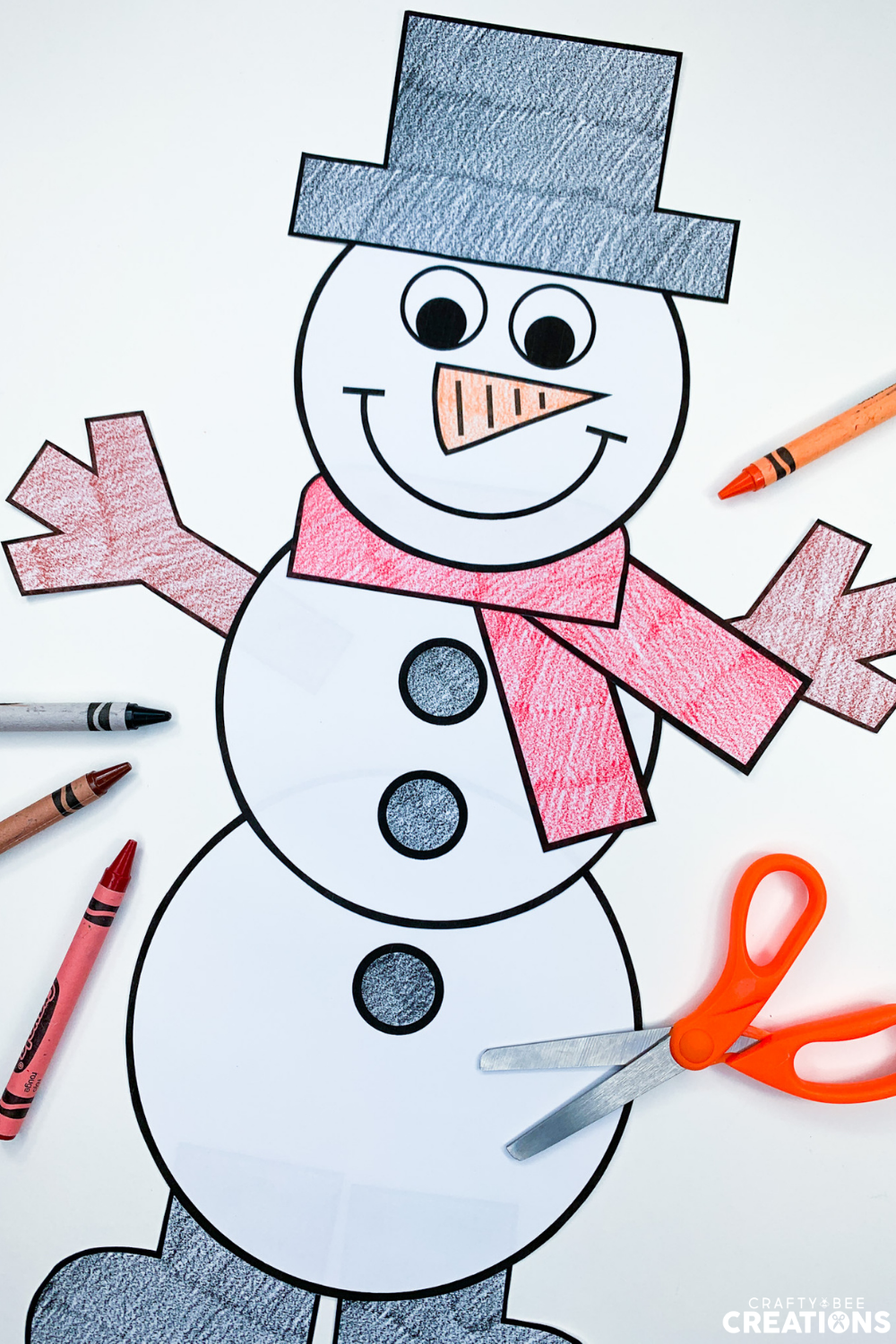 This snowman craft has been colored by a student. The scarf is red and the buttons are black. There are orange scissors as well as black, brown and red crayons lying nearby.