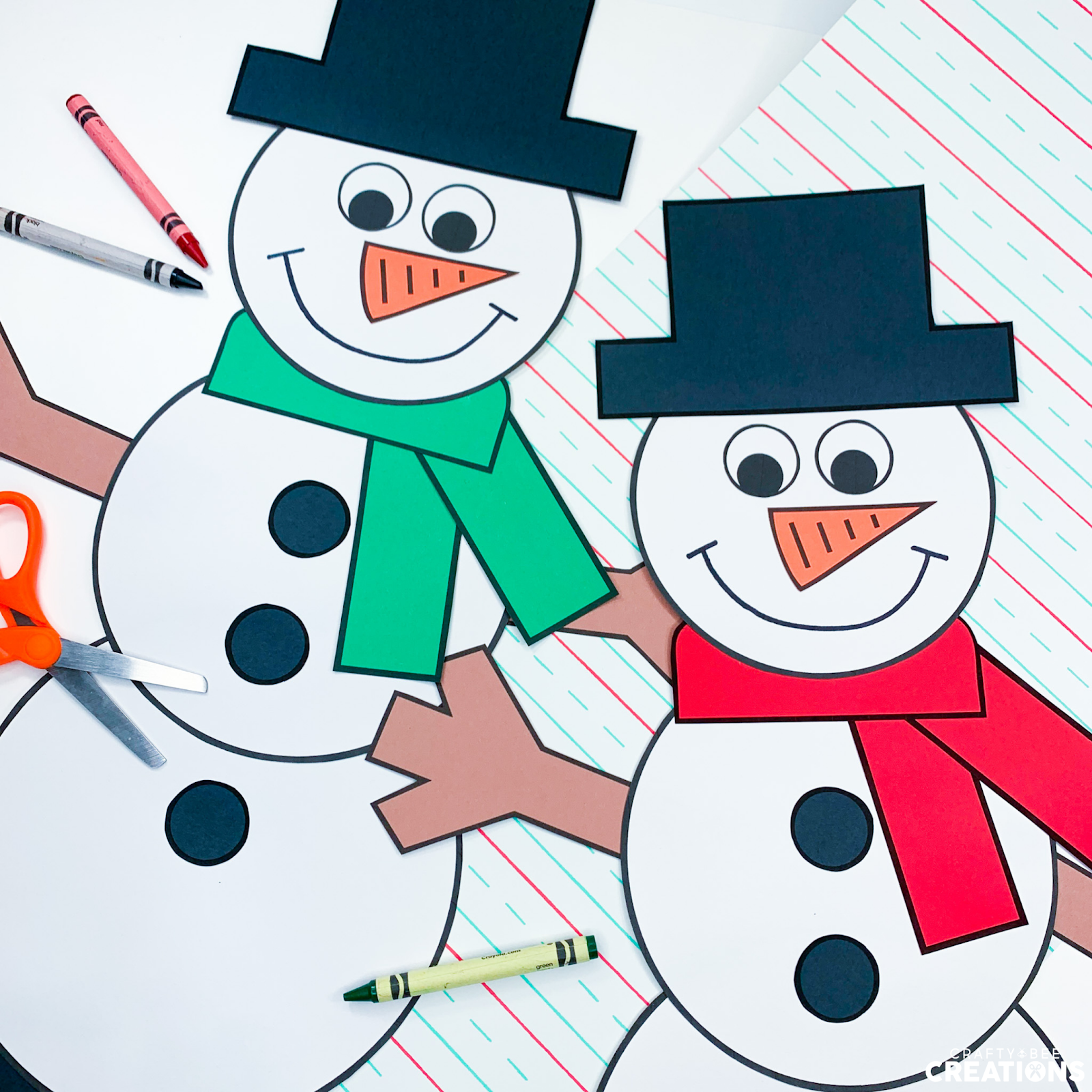 In this image there are two snowmen. One has a green scarf and the other has a red scarf. There is an orange pair of scissors as well as some multi-colored crayons laying on the table.