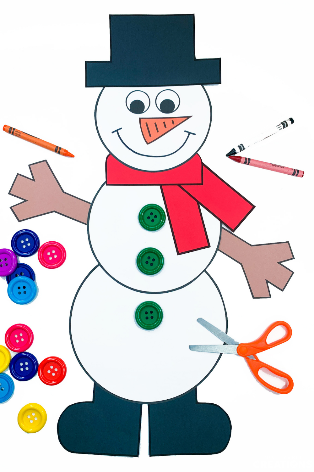This snowman craft has read green buttons on its belly. There are crayons lying on the white table beside it as well as other colored buttons. This snowman has a red scarf. A pair of orange scissors is on the page also.