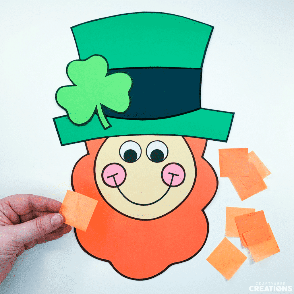 Step one of the leprechaun craft is to cut orange tissue paper into small squares.