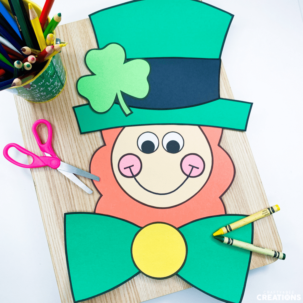 Leprechaun craft is laying on a wooden board with scissors, crayons and colored pencils.