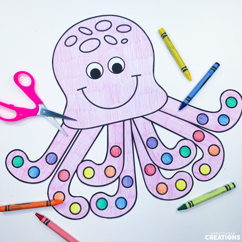 The octopus craft has been colored by a students. It's suckers are multicolored and there are many different crayons laying on the page as well as a pair of scissors.