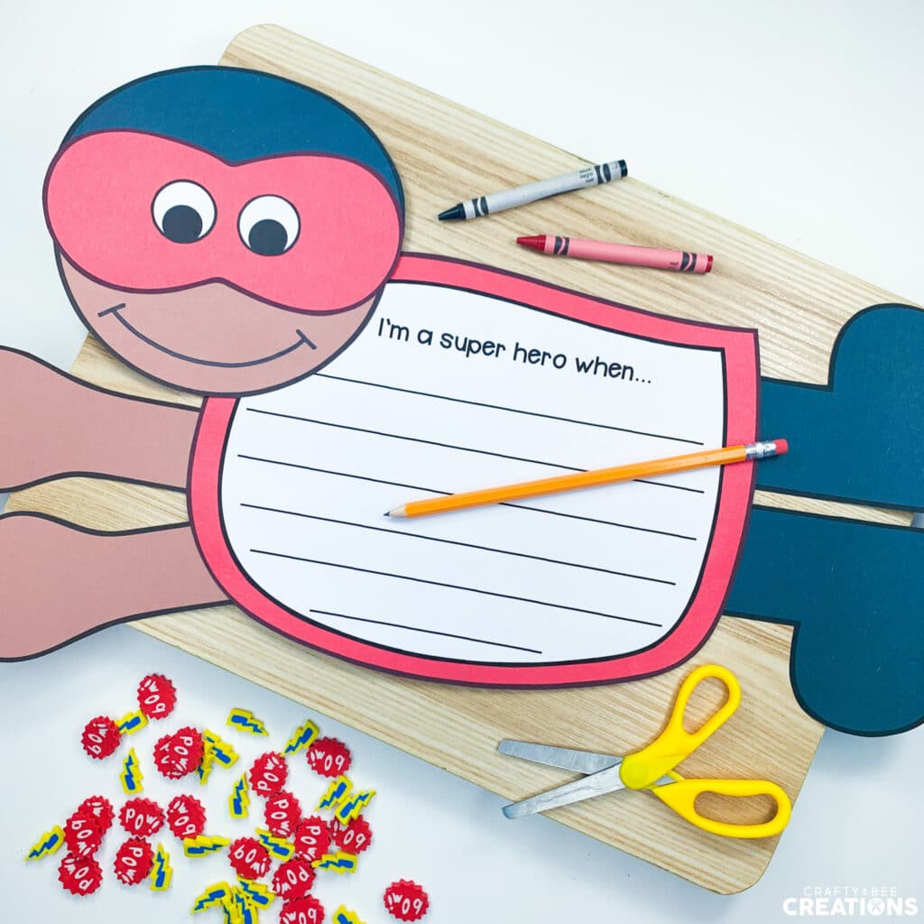 Superhero craft lies on a wooden board with crayons, scissors and superhero mini erasers.