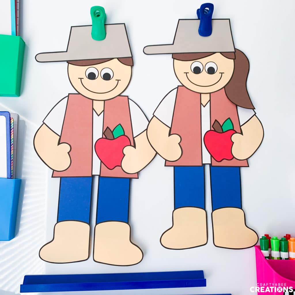Boy and girl Johnny Appleseed crafts held up by clips on a whiteboard.